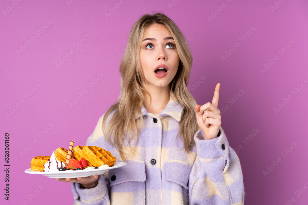 Teenager Russian girl holding waffles isolated on purple background surprised and pointing up Teenager Russian girl holding waffles isolated on purple background surprised and pointing up