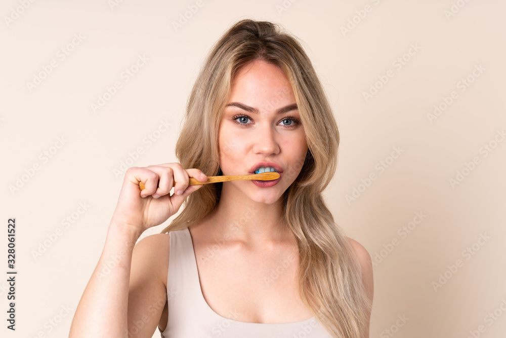 Teenager blonde girl brushing her teeth over isolated background Teenager blonde girl brushing her teeth over isolated background