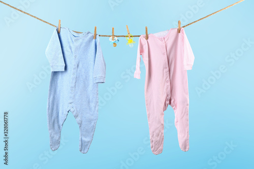 Baby clothes hanging on rope against color background