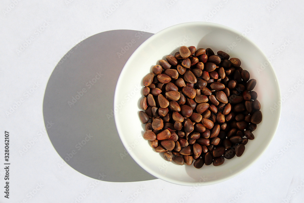 Unpeeled cedar pine nuts in a plate on white background Unpeeled cedar pine nuts in a plate on white background