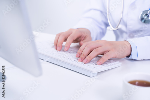 Business concept - Young female doctor woman working at office with computer  typing electronic medical record  white table background  close up  copy space