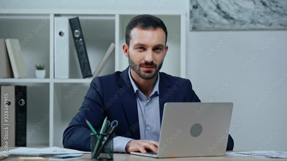 cheerful businessman typing on laptop and smiling at camera cheerful businessman typing on laptop and smiling at camera