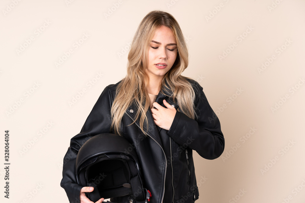 Russian girl with a motorcycle helmet isolated on beige background having a pain in the heart Russian girl with a motorcycle helmet isolated on beige background having a pain in the heart