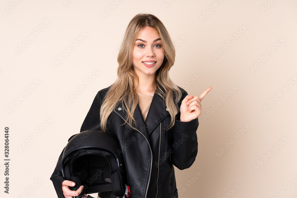 Russian girl with a motorcycle helmet isolated on beige background pointing to the side to present a product Russian girl with a motorcycle helmet isolated on beige background pointing to the side to present a product