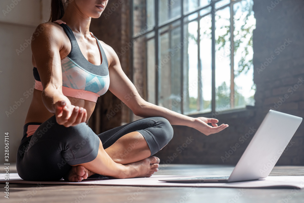 Closeup young sporty fit slim woman coach do practice video online training  hatha yoga instructor modern laptop meditate Sukhasana posture relax breathe  easy seat pose gym healthy lifestyle concept. Stock Photo