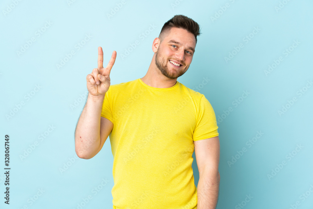 Russian handsome man isolated on blue background smiling and showing victory sign Russian handsome man isolated on blue background smiling and showing victory sign