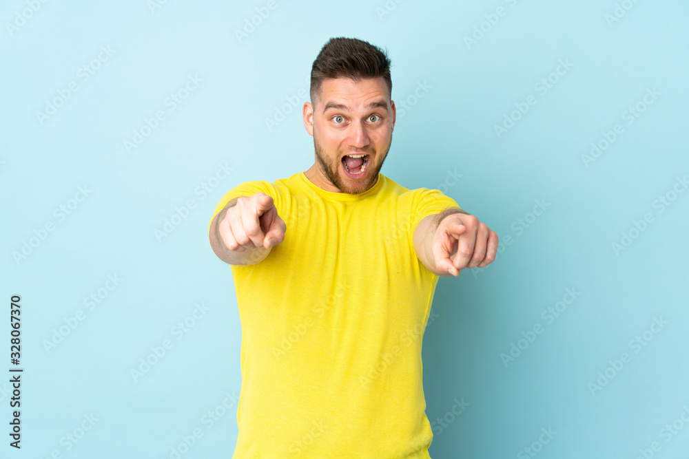 Russian handsome man isolated on blue background surprised and pointing front Russian handsome man isolated on blue background surprised and pointing front