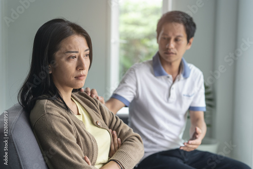 Asian couple having relation problem. Wife crying and sitting separate with her husband at home after quarrel.