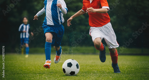 Running soccer players in duel. Youth athletes kicking black and white football ball. Junior youth soccer team compete on grass pitch. Soccer summer school tournament