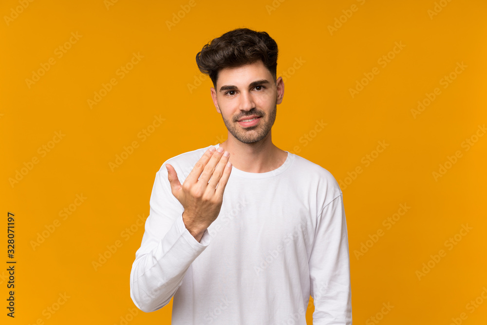 Young man over isolated orange background inviting to come with hand. Happy that you came