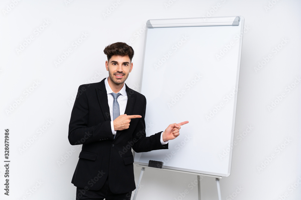 Young businessman giving a presentation on white board surprised and pointing side Young businessman giving a presentation on white board surprised and pointing side