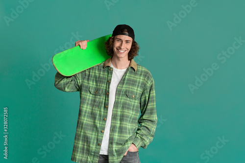 Teenage culture concept. Funky young man with skatebord on color background, space for text photo