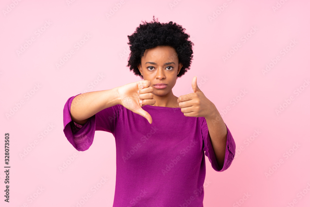 African american woman over isolated pink background making good-bad sign. Undecided between yes or not African american woman over isolated pink background making good-bad sign. Undecided between yes or not