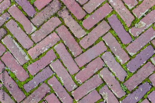 Old reddish tiles with moss between herringbone tile background pattern
