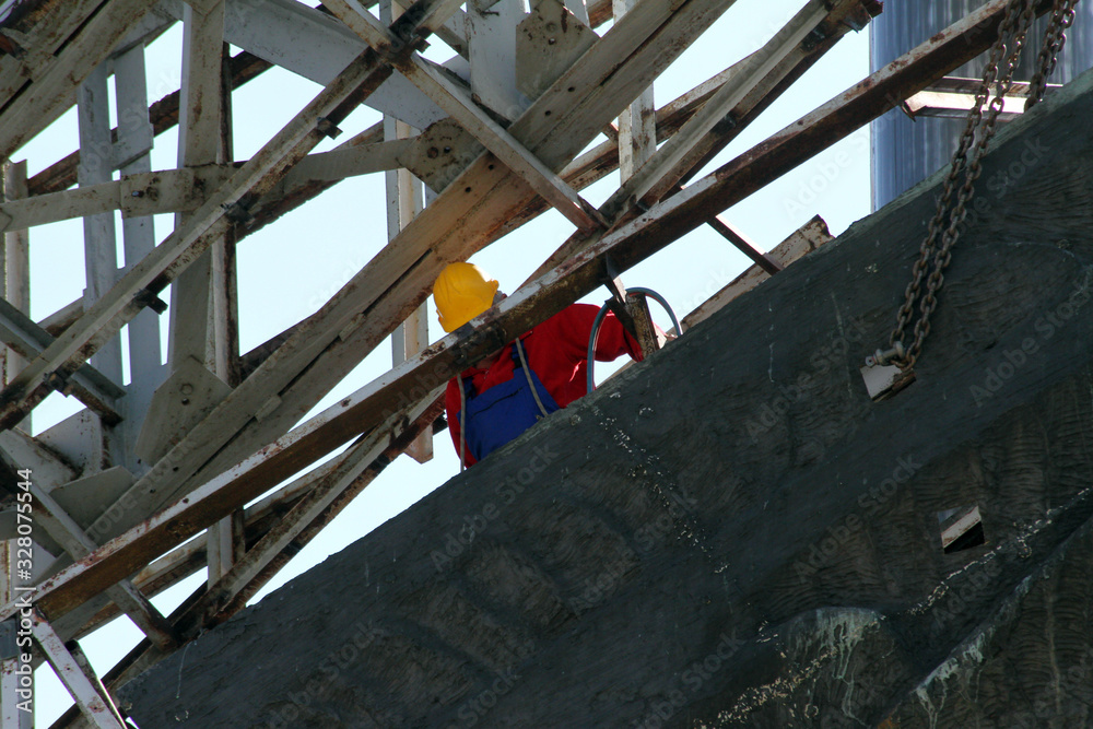 Performing heavy construction work. A worker climbs in height and dismantles large steel elements.