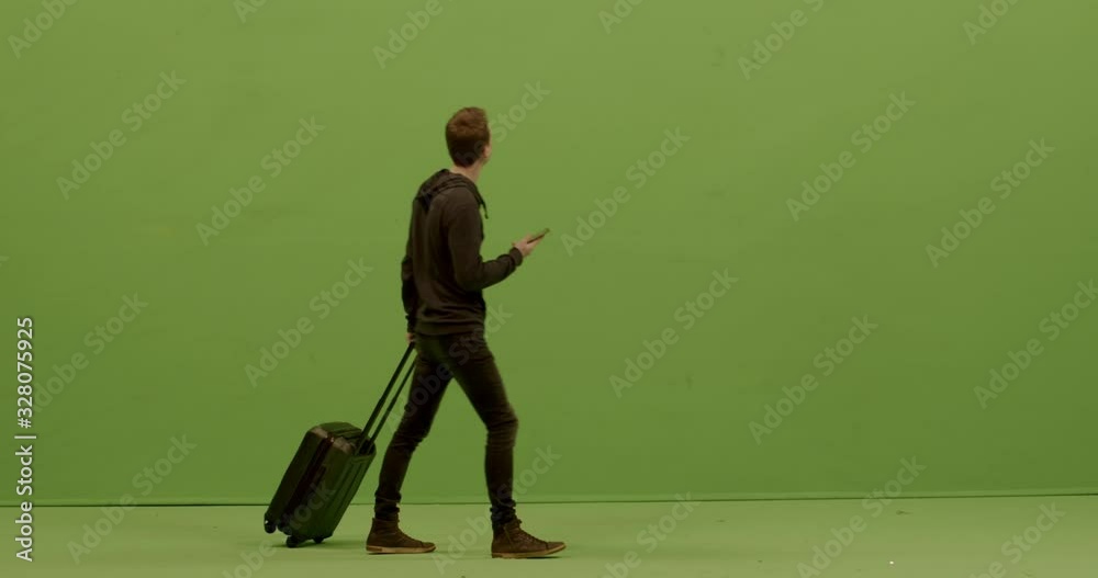 GREEN SCREEN CHROMA KEY FULL SHOT Caucasian male checking his phone, walking with suitcase in the airport or train station