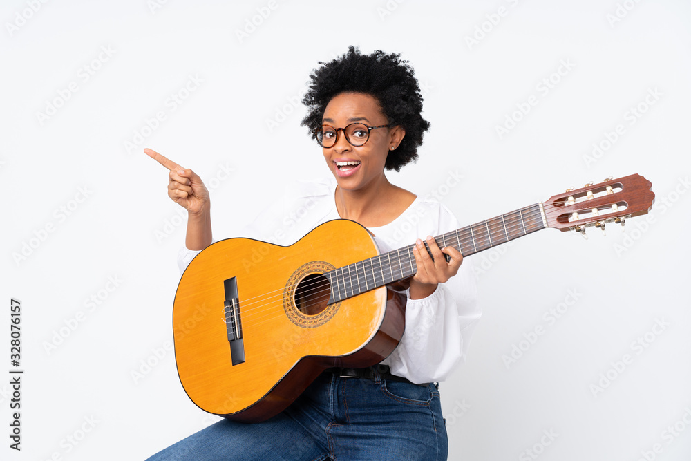 Obraz premium African american woman with guitar over isolated background surprised and pointing side