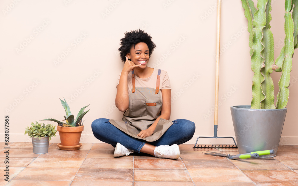Gardener woman sitting on the floor making phone gesture. Call me back sign Gardener woman sitting on the floor making phone gesture. Call me back sign