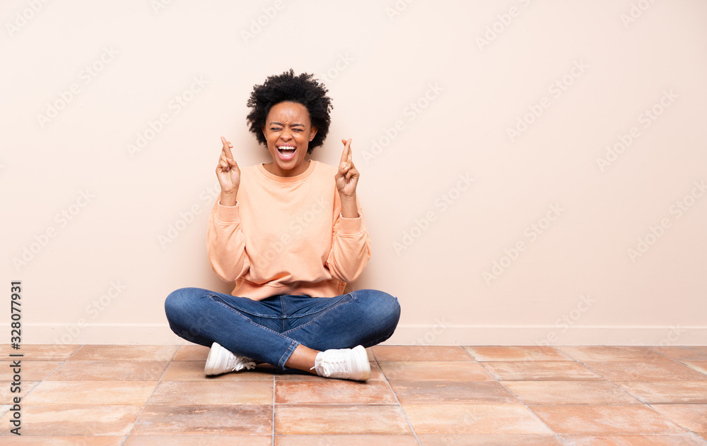 African american woman sitting on the floor with fingers crossing African american woman sitting on the floor with fingers crossing