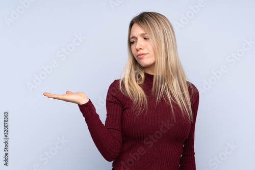 Young blonde woman over isolated blue background holding copyspace with doubts