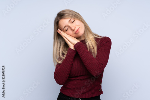 Young blonde woman over isolated blue background making sleep gesture in dorable expression © luismolinero