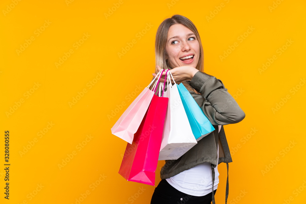 Young blonde woman over isolated yellow background holding shopping bags and smiling Young blonde woman over isolated yellow background holding shopping bags and smiling