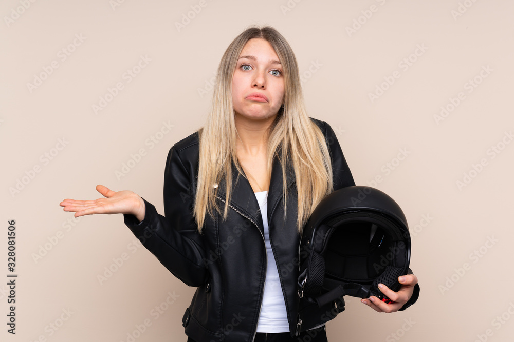 Young blonde woman with a motorcycle helmet over isolated background having doubts with confuse face expression Young blonde woman with a motorcycle helmet over isolated background having doubts with confuse face expression