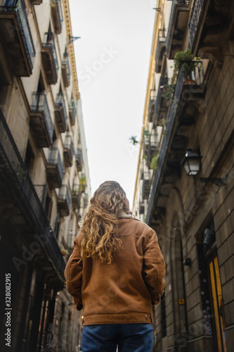 Blond girl walking through the streets of the center of the city of Barcelona in Catalonia, Spain wearing a jacket and blue jeans. Looking up to the old buldings.