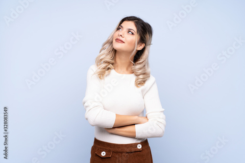 Young teenager girl over isolated blue background looking up while smiling