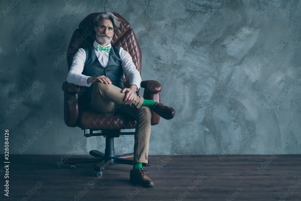 Full length photo of smart masculine old company owner man sit armchair look modern wear green dotted bow-tie socks hairstyle isolated concrete wall grey color background