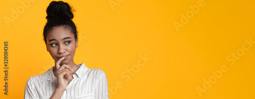 Doubtful afro girl thinking about something, looking away on yellow background