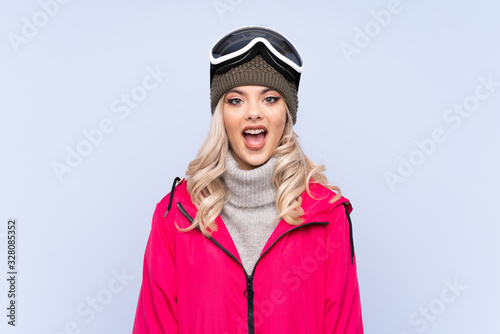 Skier teenager girl with snowboarding glasses over isolated blue background with surprise facial expression © luismolinero