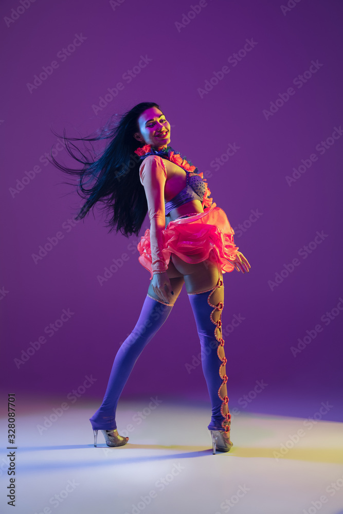 Fototapeta Motion, flying hairs. Hawaiian brunette model on purple studio background in neon light. Beautiful women in traditional clothes smiling and having fun. Bright holiday's, celebration colors, festival.