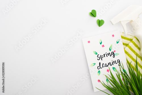 top view of green grass and cleaning supplies near spring cleaning card on white background