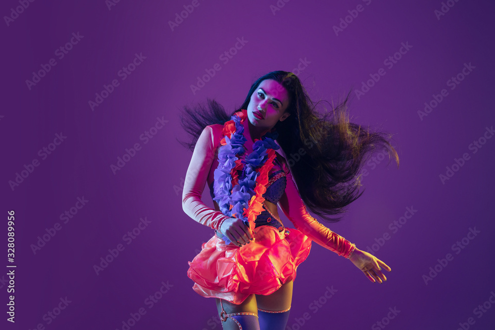 Motion, flying hairs. Hawaiian brunette model on purple studio background in neon light. Beautiful women in traditional clothes smiling and having fun. Bright holiday's, celebration colors, festival.