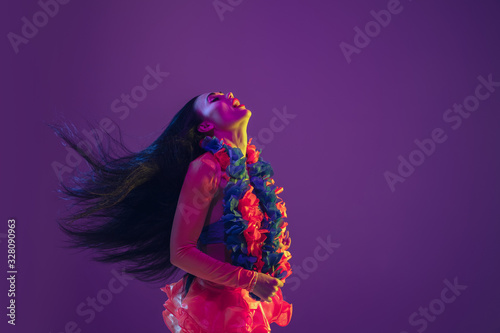 Motion, flying hairs. Hawaiian brunette model on purple studio background in neon light. Beautiful women in traditional clothes smiling and having fun. Bright holiday's, celebration colors, festival. photo