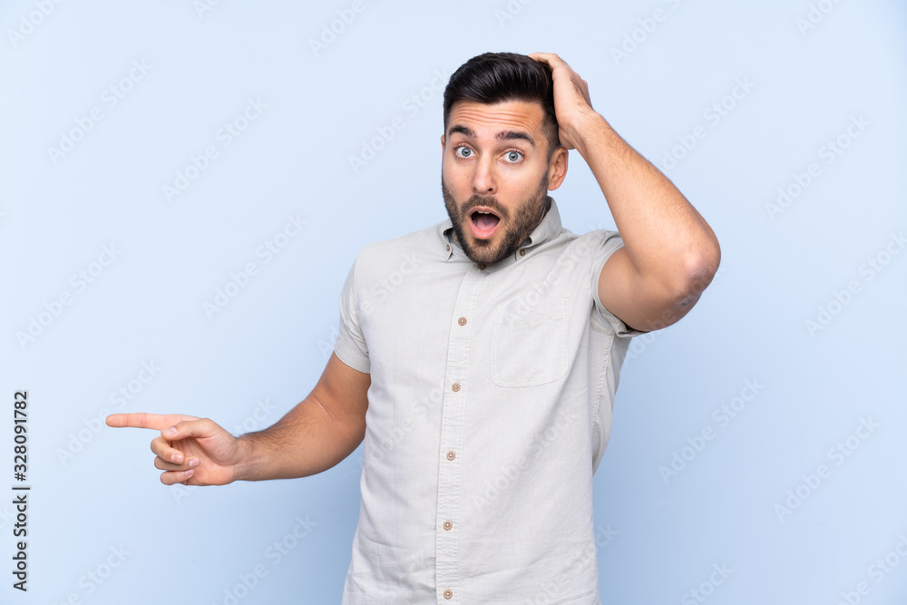 Young handsome man with beard over isolated blue background surprised and pointing finger to the side Young handsome man with beard over isolated blue background surprised and pointing finger to the side