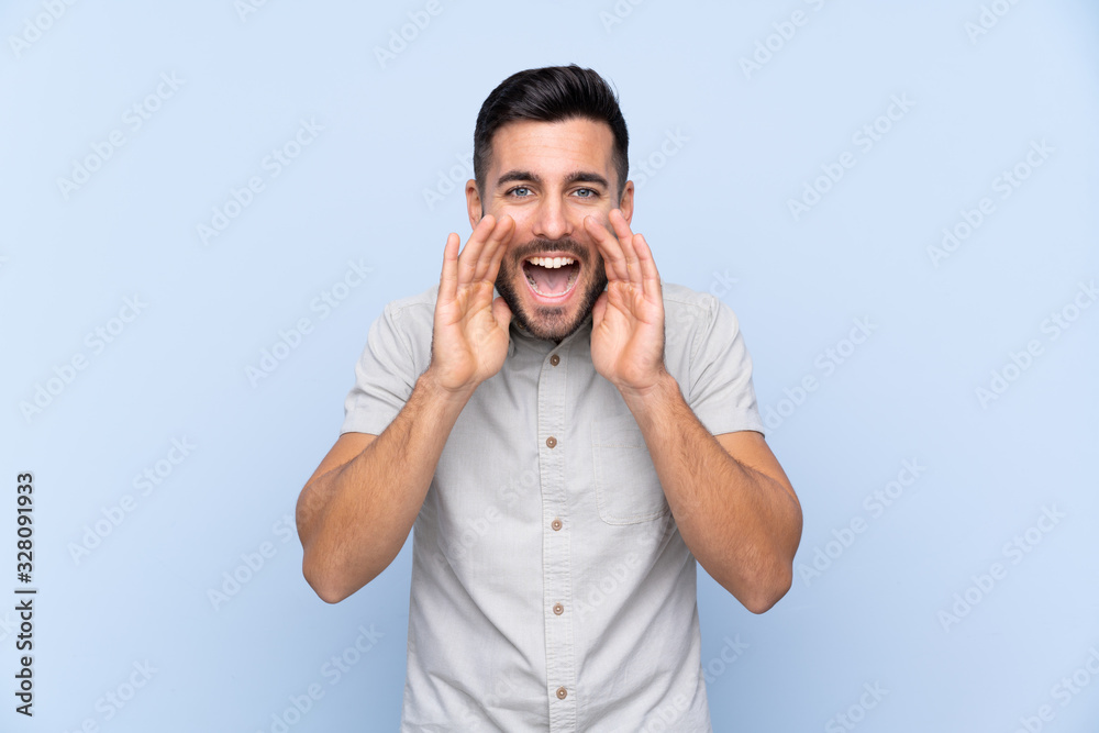 Young handsome man with beard over isolated blue background shouting with mouth wide open Young handsome man with beard over isolated blue background shouting with mouth wide open