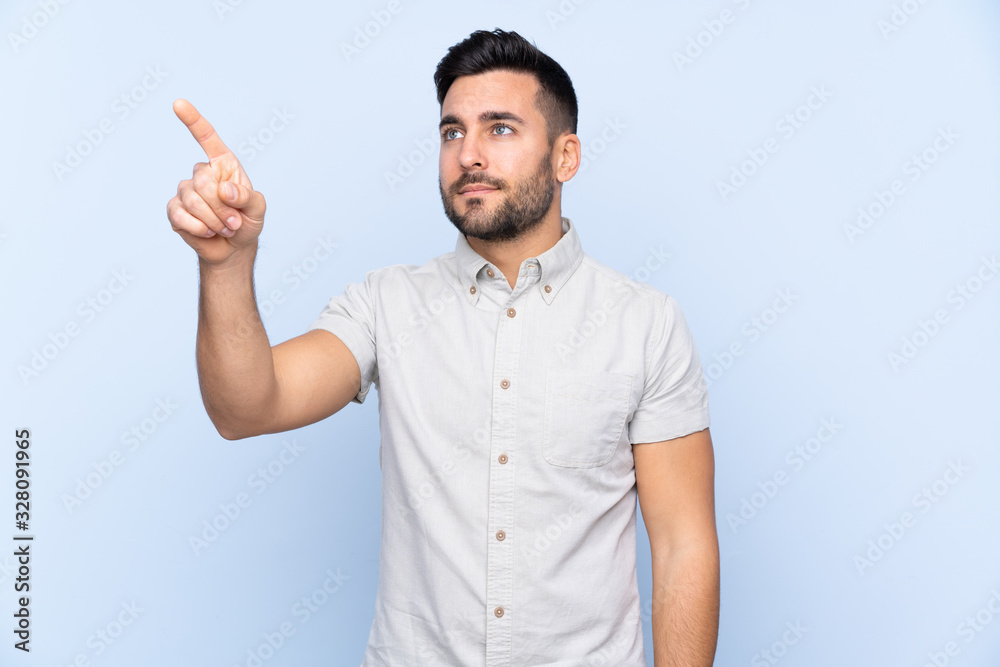 Young handsome man with beard over isolated blue background touching on transparent screen Young handsome man with beard over isolated blue background touching on transparent screen