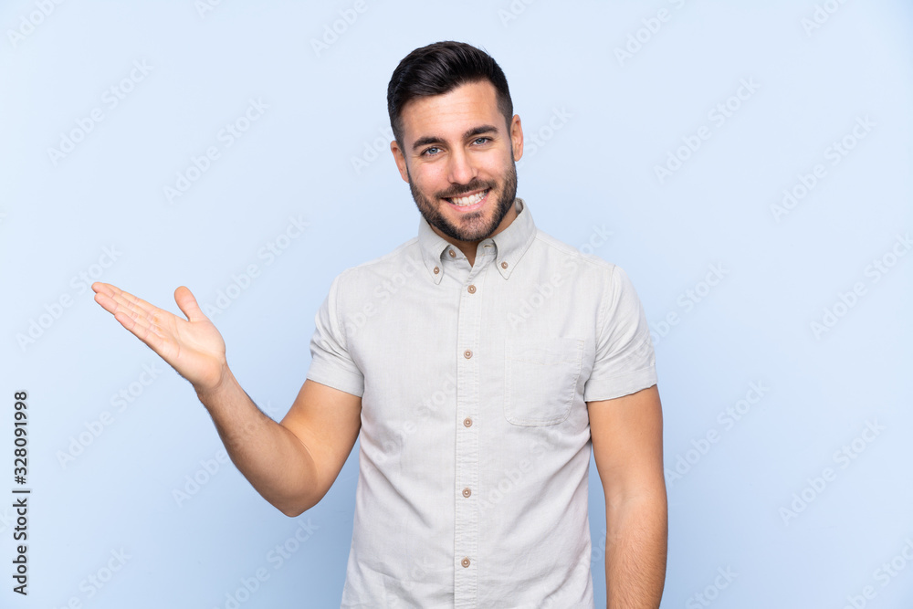 Young handsome man with beard over isolated blue background holding copyspace imaginary on the palm Young handsome man with beard over isolated blue background holding copyspace imaginary on the palm
