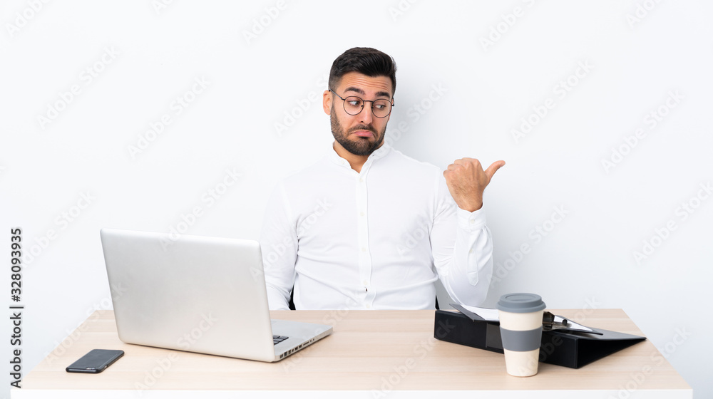 Young businessman in a workplace unhappy and pointing to the side