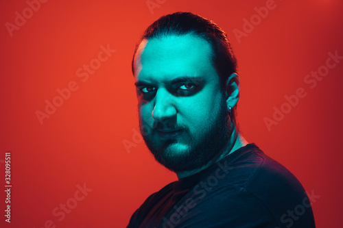 Portrait of a guy with colorful neon light on red studio background. Male model with calm and serious mood. Facial expression, cyberpunk, millenials lifestyle and look like. Future, technologies.