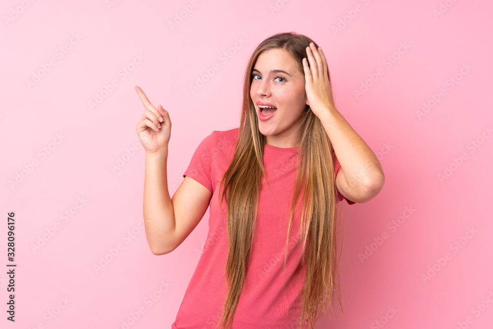 Teenager blonde girl over isolated pink background surprised and pointing finger to the side Teenager blonde girl over isolated pink background surprised and pointing finger to the side