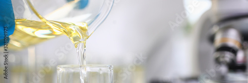 Scientist hand wearing protective gloves pouring some yellow liquid at laboratory