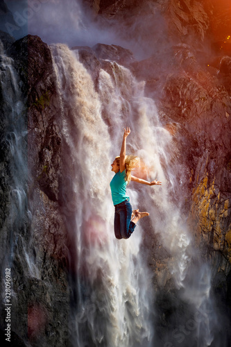 Eine Frau springt vor Freude vor einem Wasserfall