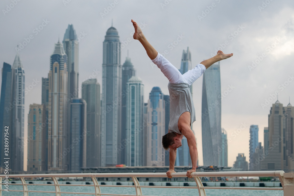 Muscular man doing workout on the street with cityscape of skyscrapers on background in Dubai. Concept of healthy lifestyle and modern