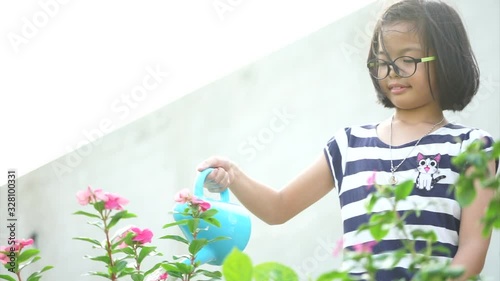 Little Asian girl watering the flower plant by watering can in the sunny day.