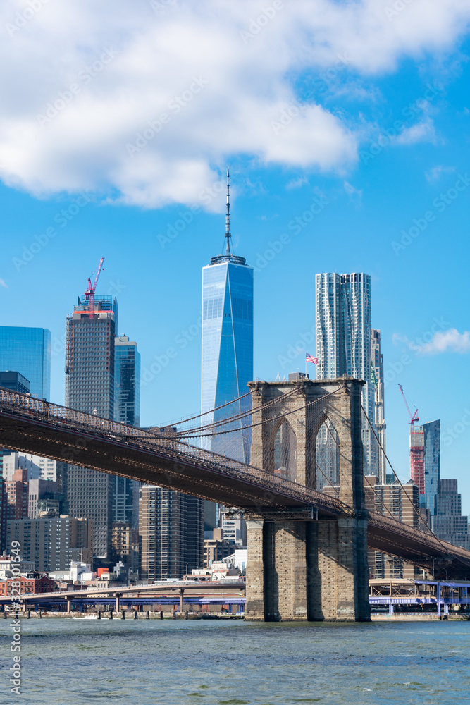 The Brooklyn Bridge with an American Flag over the East River with the Lower Manhattan New York City Skyline