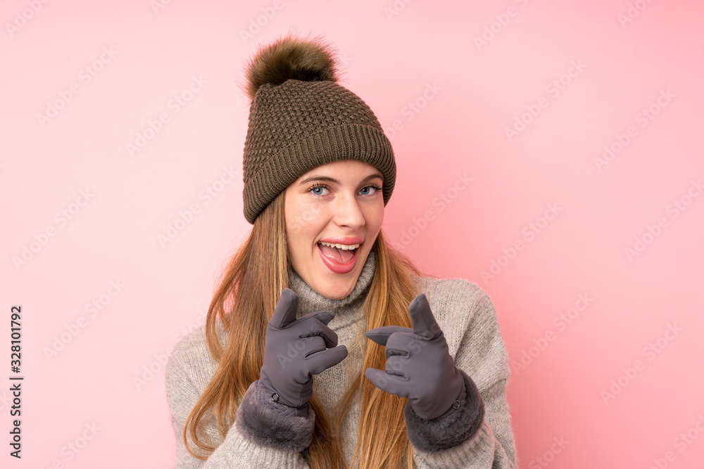 Young teenager girl with winter hat over isolated pink background points finger at you
