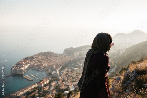 Portrait of Woman with hijab standing above old city of Dubrovnik. She is happy and relaxed. She is enjoying sunset. 